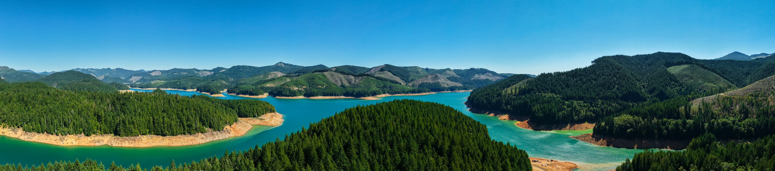Aerial panorama of Foster Reservoir, Oregon — turquoise water winding between forested ridges under a clear summer sky