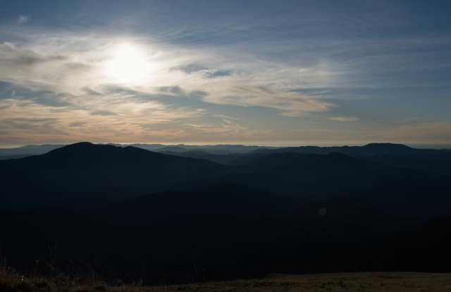 The moon hanging over dark, layered mountains at dusk