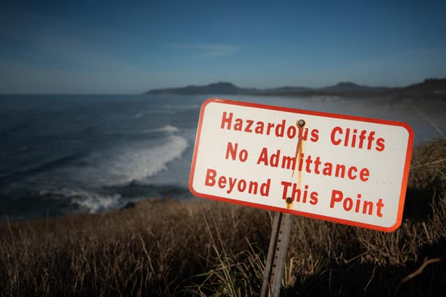 A weathered 'Hazardous Cliffs' sign above a churning coastline