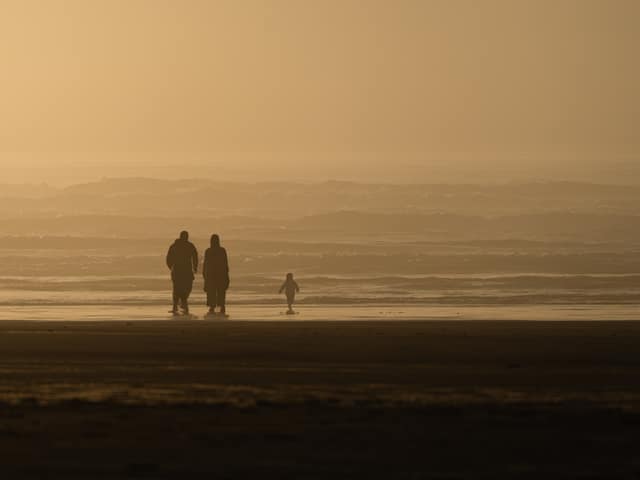 Two figures and a child silhouetted on a hazy golden beach