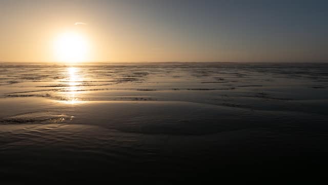 Low sun glinting across wet sand at sunrise