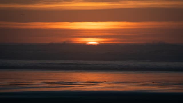 The sun sinking into the ocean in bands of orange