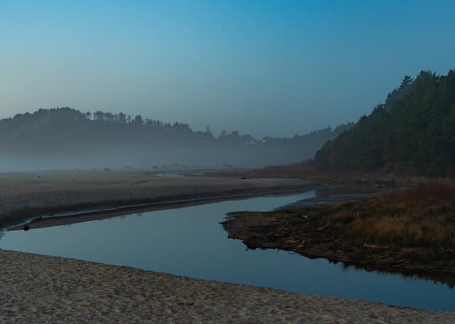 A tidal channel curving through a misty estuary at first light