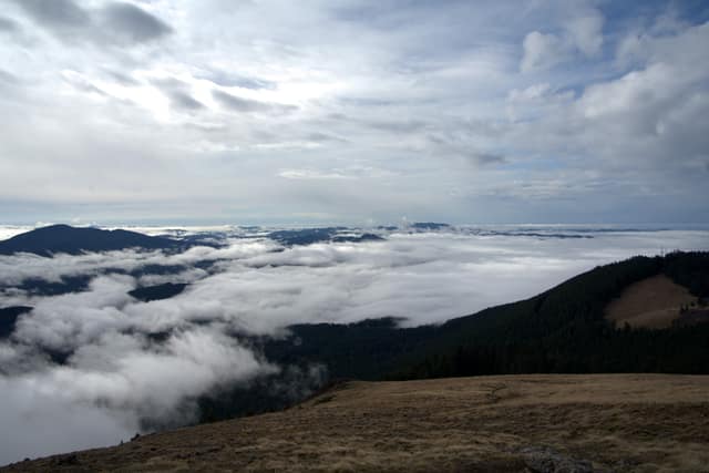 A sea of clouds filling the valleys below a grassy summit