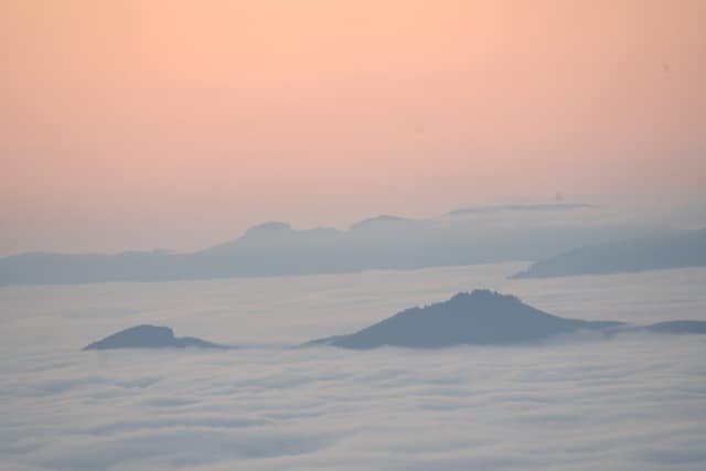 A pastel pink sky over a sea of clouds, distant peaks poking through