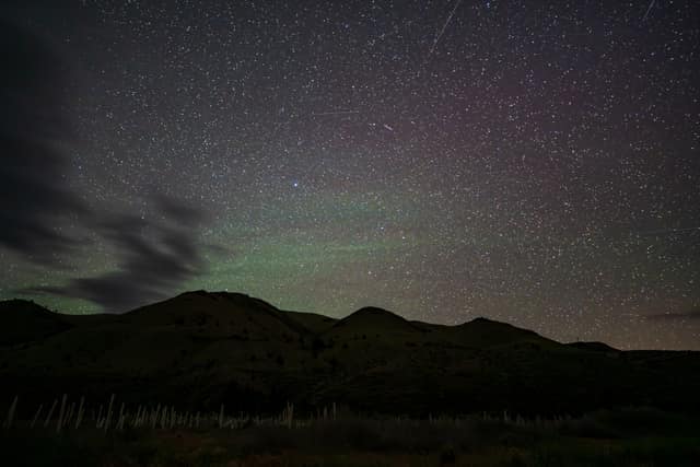 Faint green aurora and stars over darkened desert hills