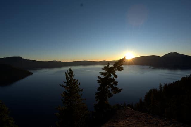Sunrise over Crater Lake, framed by silhouetted conifers