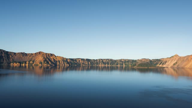Golden evening light on Crater Lake's caldera rim, mirrored in glassy blue water
