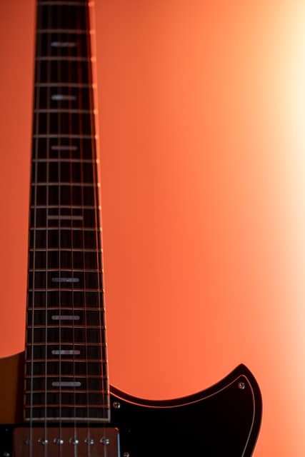 The neck and fretboard of an electric guitar against a warm orange backdrop