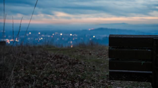 A hilltop bench looking out over distant city lights at dusk