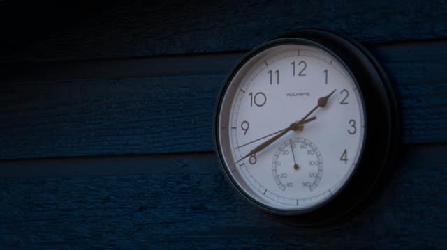 A round wall clock mounted on weathered blue siding