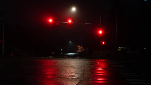 Red traffic lights reflected on a rain-slicked road at night