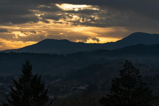 Golden light breaking over forested hills at sunset