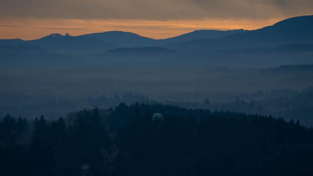 A water tower silhouetted against layered dusk hills